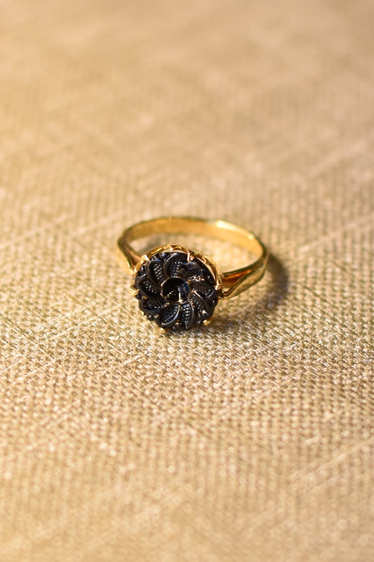 Gold ring with ornate black stone setting on beige textured fabric background