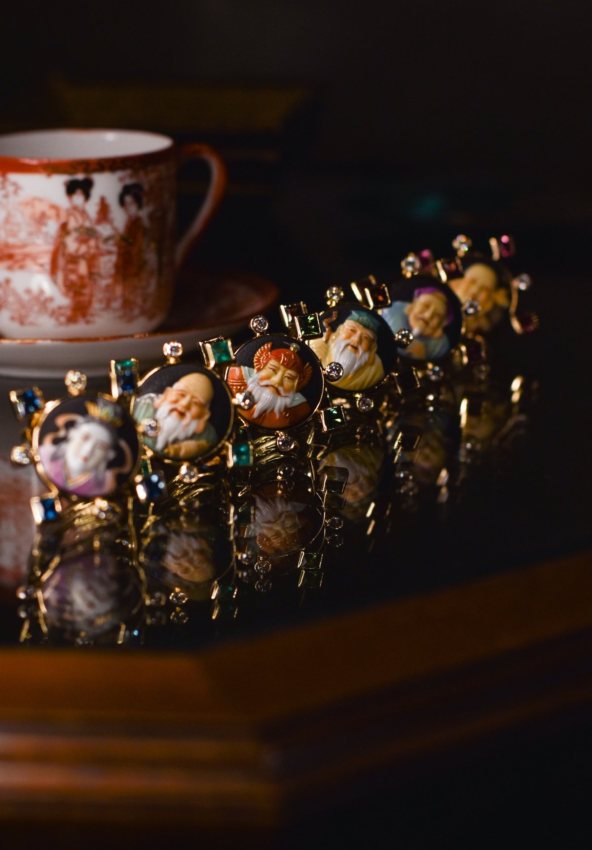 Row of ornate gold and porcelain figurines with painted faces, displayed against a dark background with a decorative ceramic pitcher behind