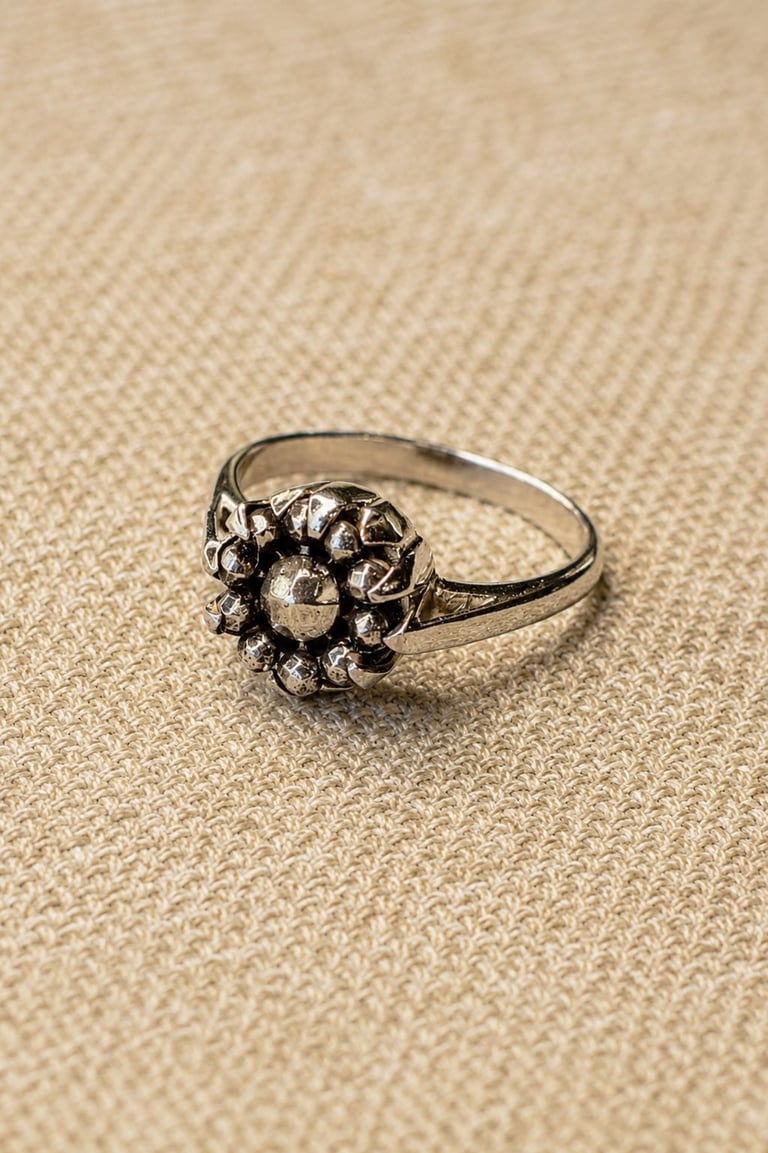 Ornate silver ring with decorative floral cluster design on beige textured fabric background